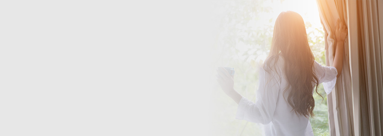 Donna che guarda fuori mentre tiene le tende.